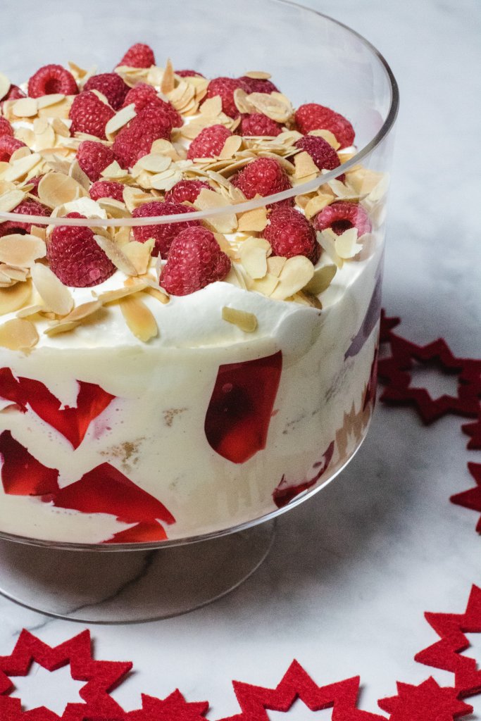 Raspberry trifle in a trifle bowl on a white marble background with a red christmas decoration in the background