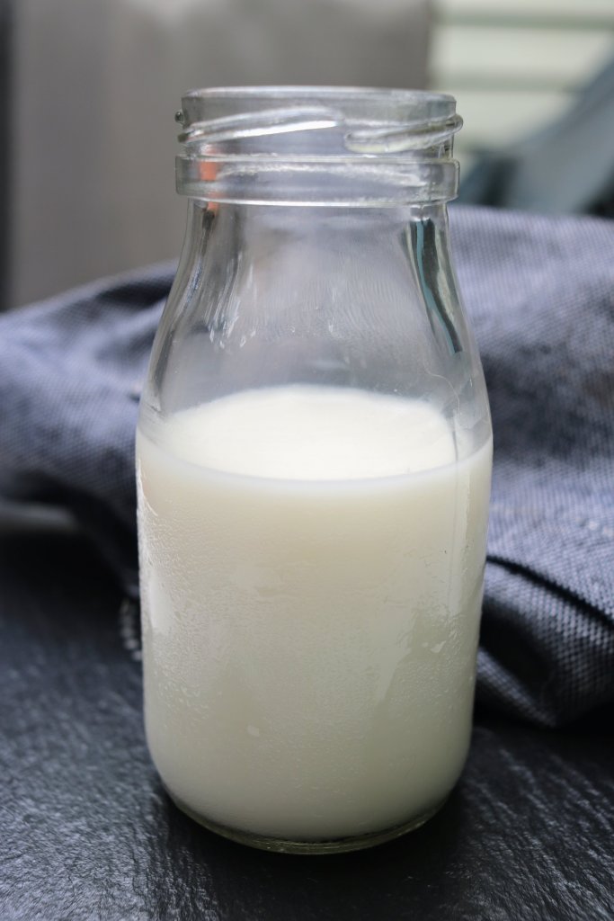 Almond milk in a glass bottle with grey linen tea towel in the background