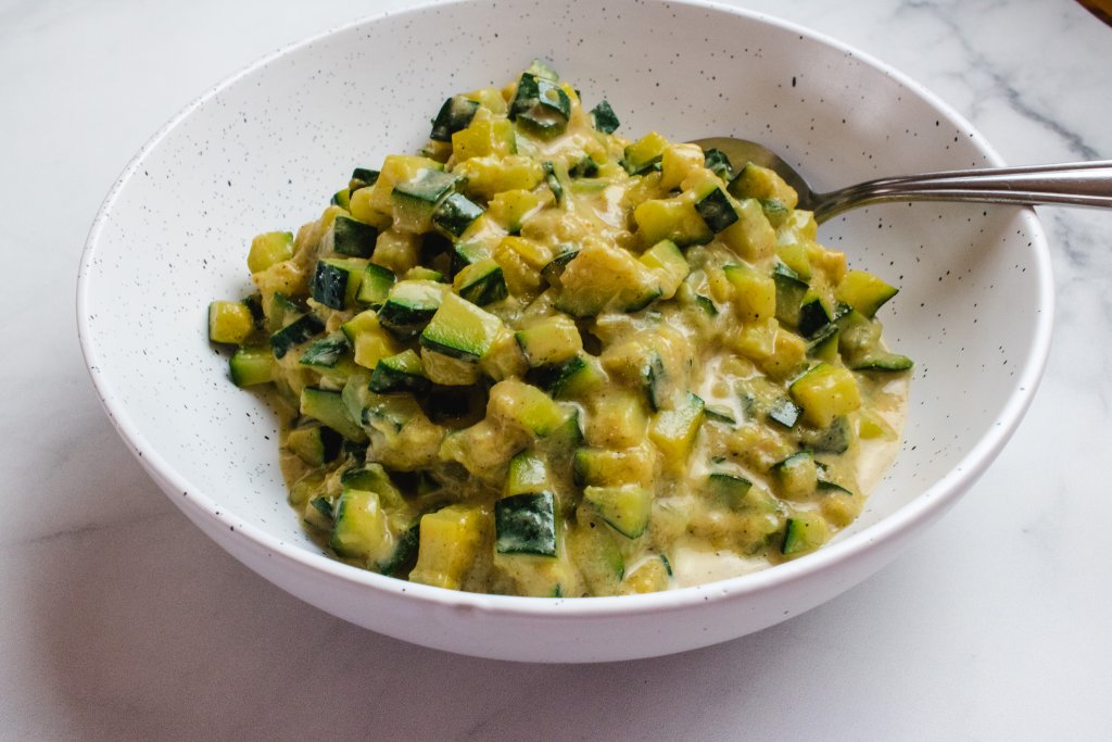 Curried zucchini in a while and black speckled bowl with a silver spoon sitting in it. 
