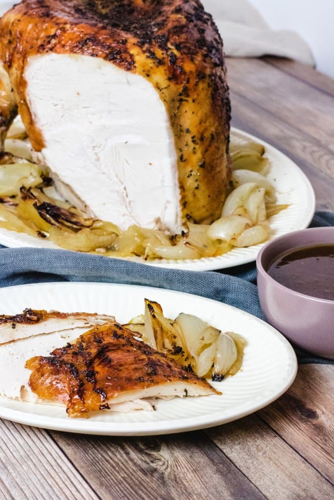 Cooked turkey buffe on a white plate with cooked onion, with cherry sauce in a bowl in front. Some sliced turkey on a white plate with some onions