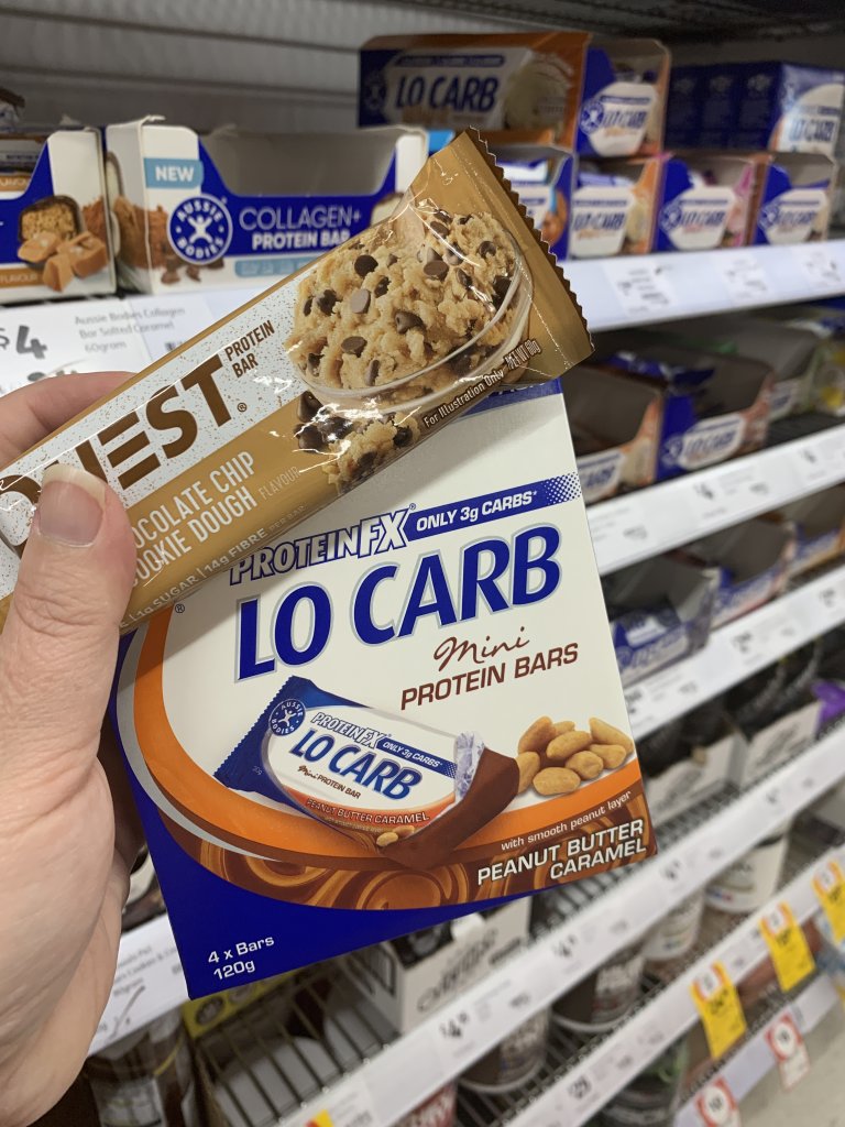 Hand holding quest and lo carb protein bars. A perfect keto snack at Coles