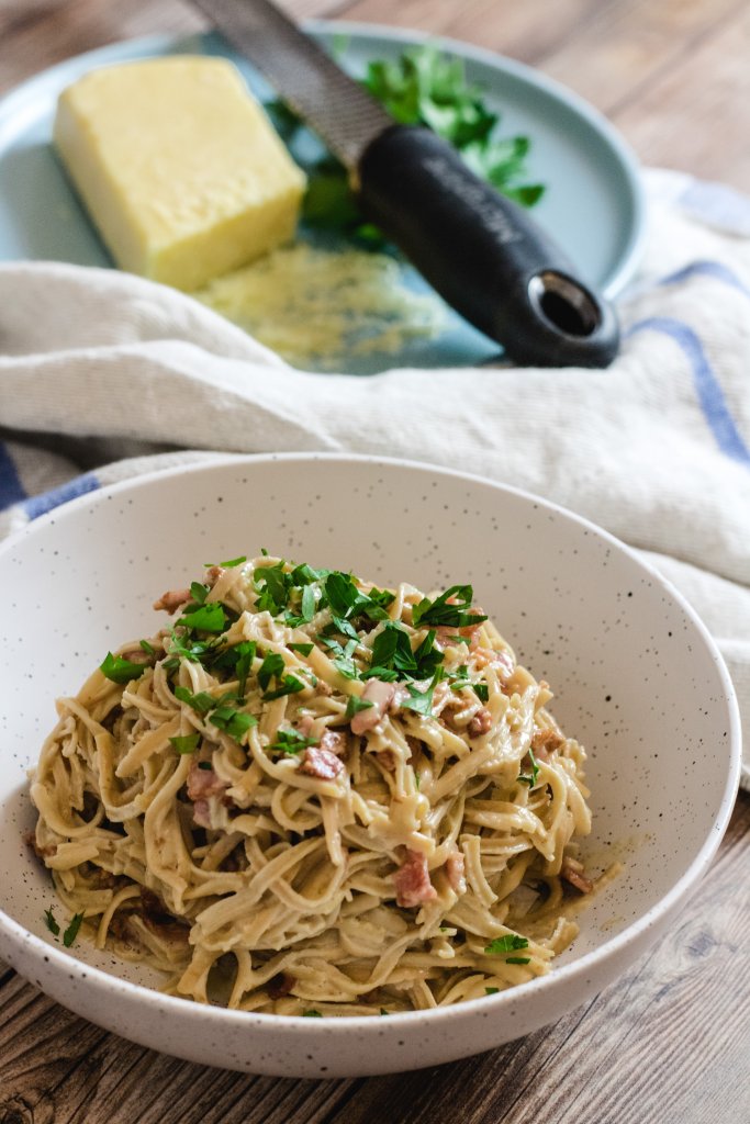 keto carbonara in a white speckled bowl with parmesan cheese and parsley on a plate in the background