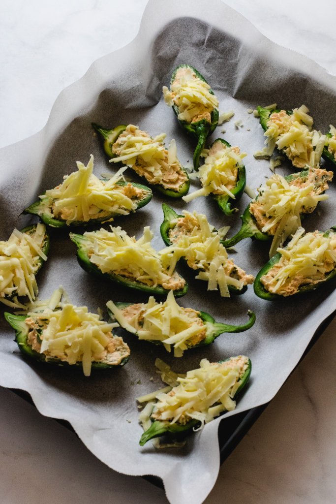 Uncooked jalapeno poppers on a baking tray with baking paper underneath