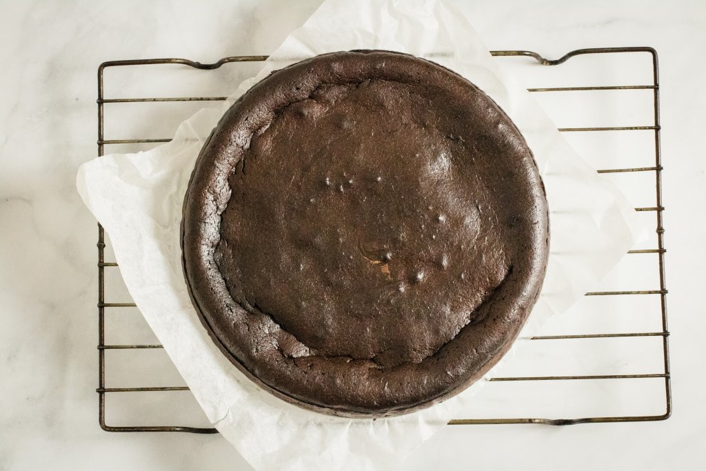 Keto flourless chocolate cake on a wire cooling rack on a white marble background