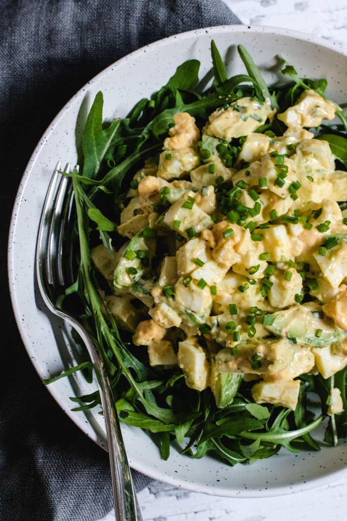 Keto egg salad sitting on a bed of rocket in a whiite speckled bowl