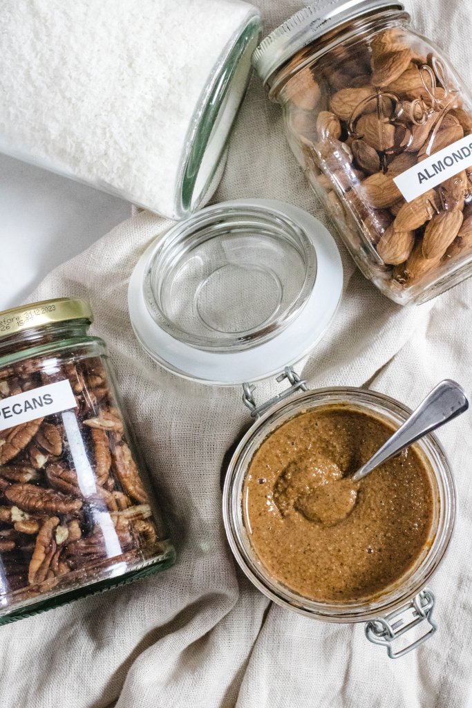 Coconut, almonds and pecans in jars on a marbeled background with a jar of almond butter