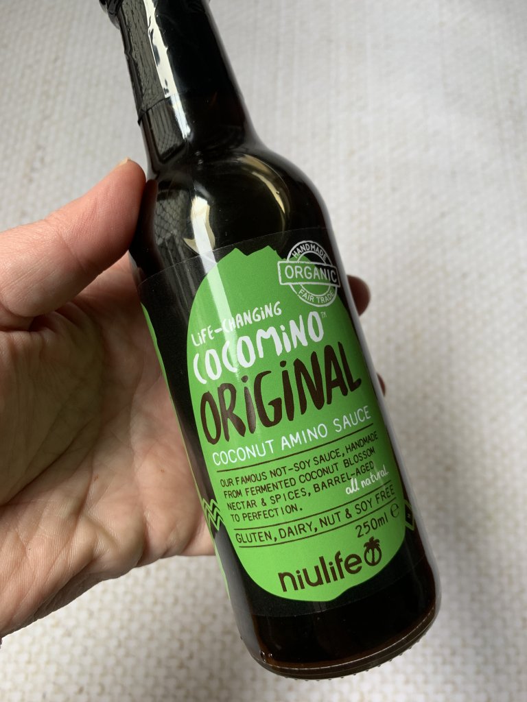 A bottle of Niulife coconut aminos held in a hand