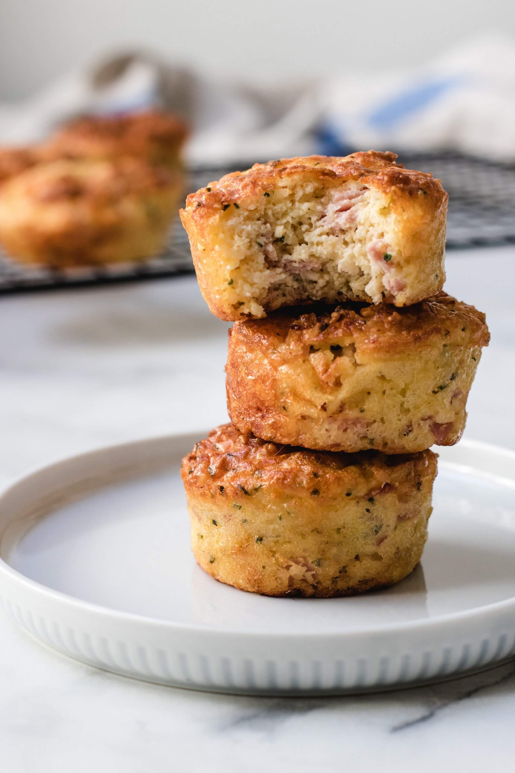 A stack of ham and cheese muffins on a plate, the top one has a bit then out.