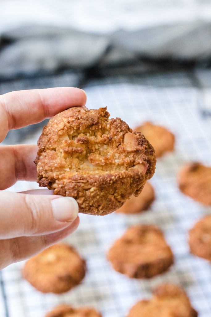 A hand holding an Anzac biscuit with more Anzac biscuits on a cooling rack in the background