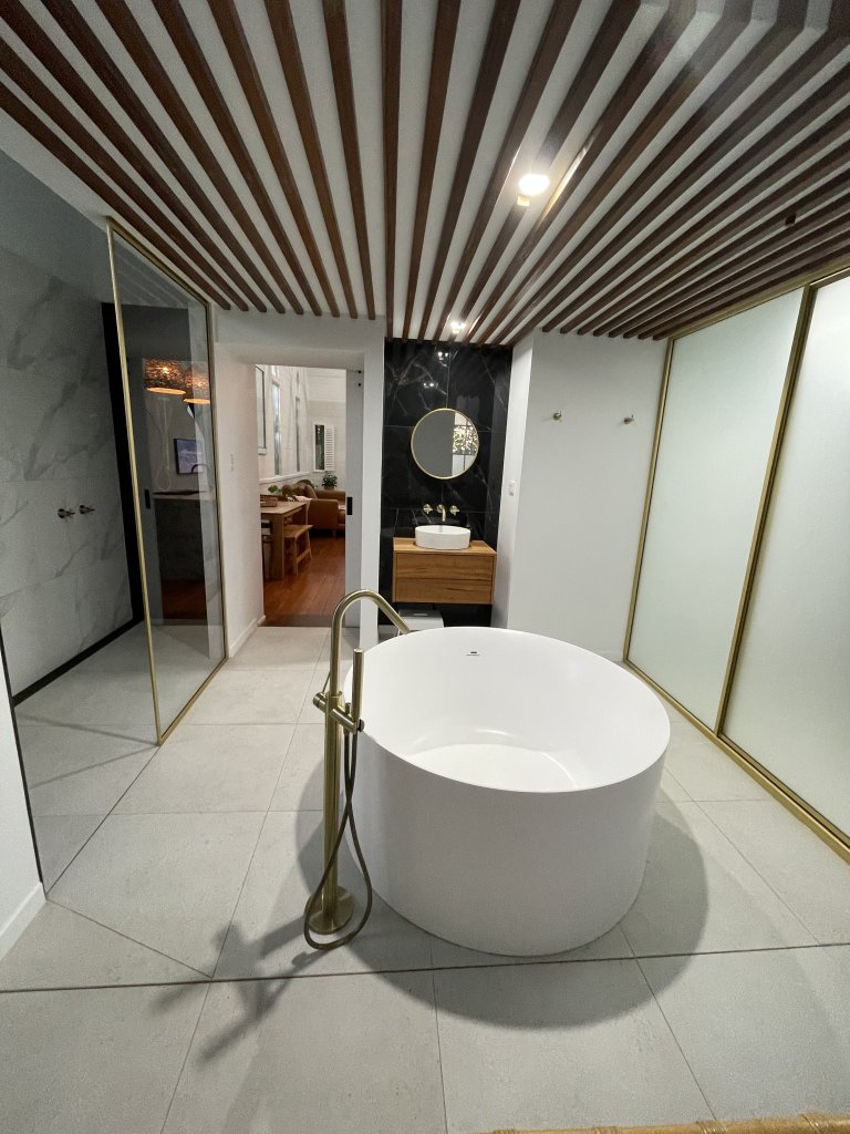 Bathroom with a large white round bathtub in the middle of the room with a shower screen to the left and a vanity a tthe bacj