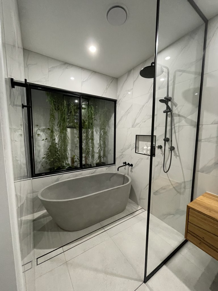 Bathroom with a large gray concrete bath and a black shower head