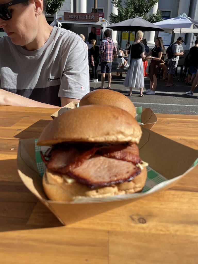 2 bacon and egg rolls on a wooden table with people in the background
