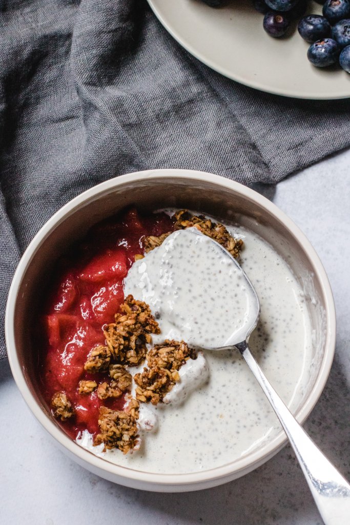 Protein chia pudding in a white round bowl with strawberry compote and granola and a silver spoon with some chia pudding on it 
