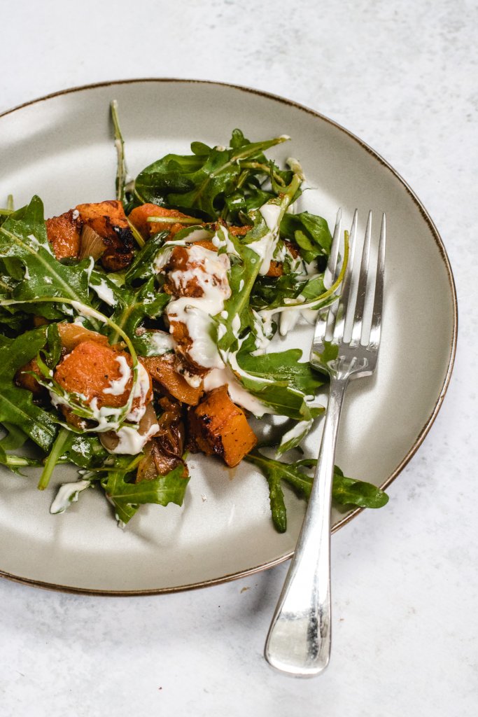 Roasted pumpkin salad on a beige round plate with a silver fork to the side on a white background. 