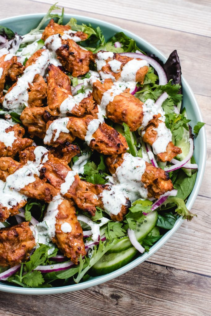 Tandoori chicken salad in a light green bowl on a wooden background