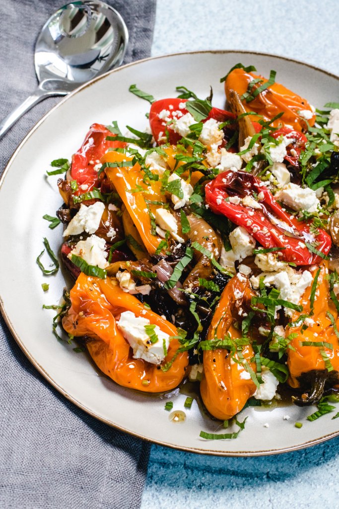 Roasted peppers salad on a beige round plate with a silver spoon beside the palte