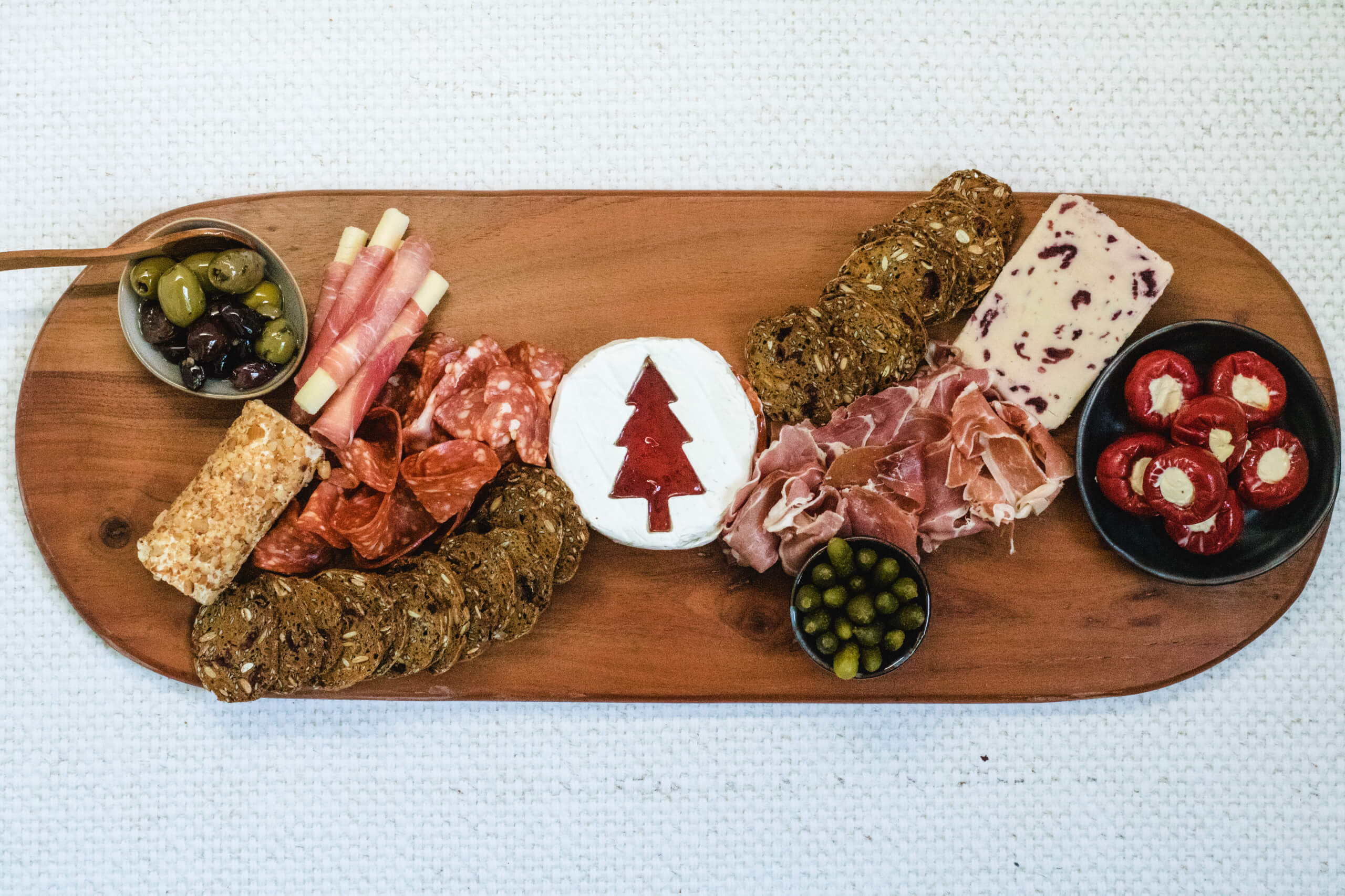 Charcuterie board with the Brie with a Christmas tree cut into it with strawberry jam filling the Christmas tree, wensleydale cheese and apple and cinnamon cheese placed on the board and a line of crackers from the cheese. Added deli meats, olives in small dishes and stuffed capsicums. 