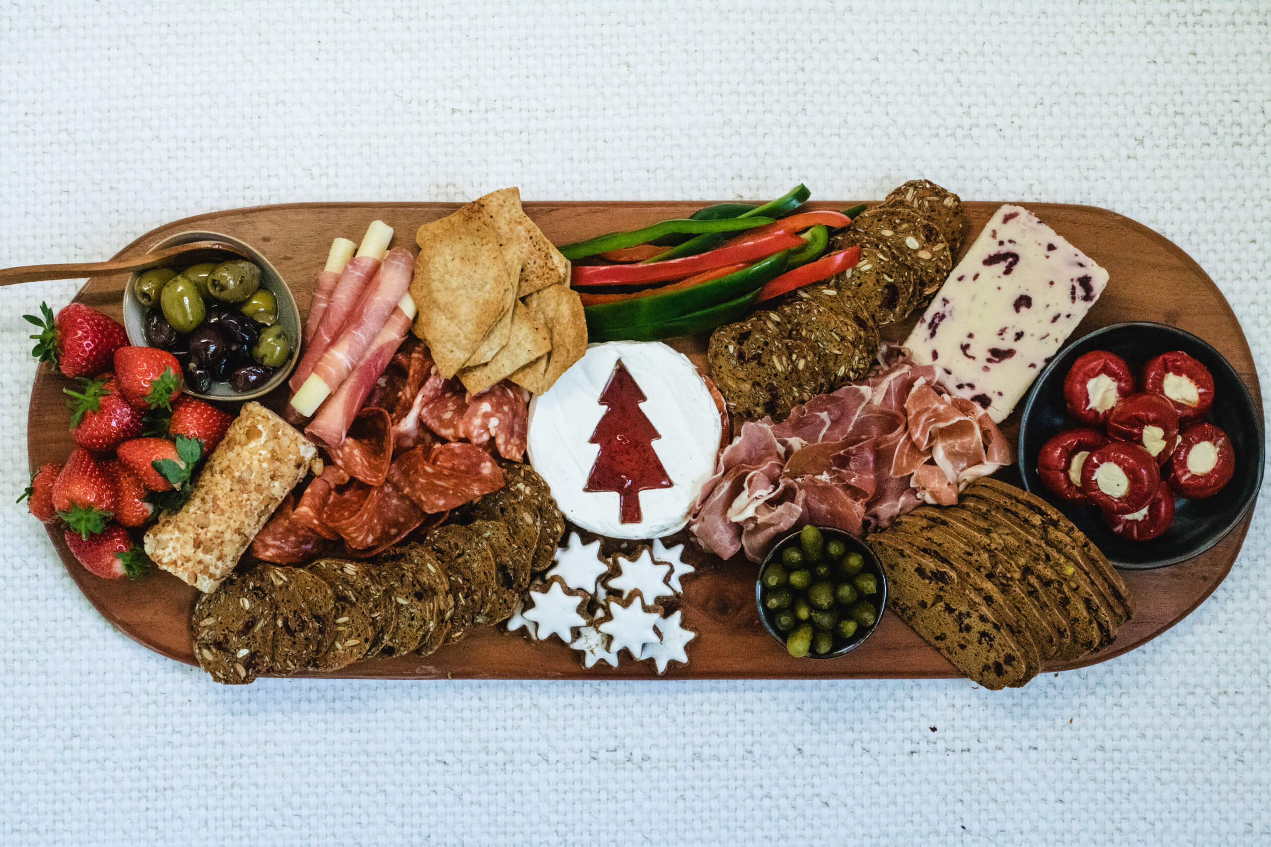 Charcuterie board with the Brie with a Christmas tree cut into it with strawberry jam filling the Christmas tree, wensleydale cheese and apple and cinnamon cheese placed on the board and a line of crackers from the cheese. Added deli meats, olives in small dishes and stuffed capsicums. Added capsicums, crackers and cookies. 