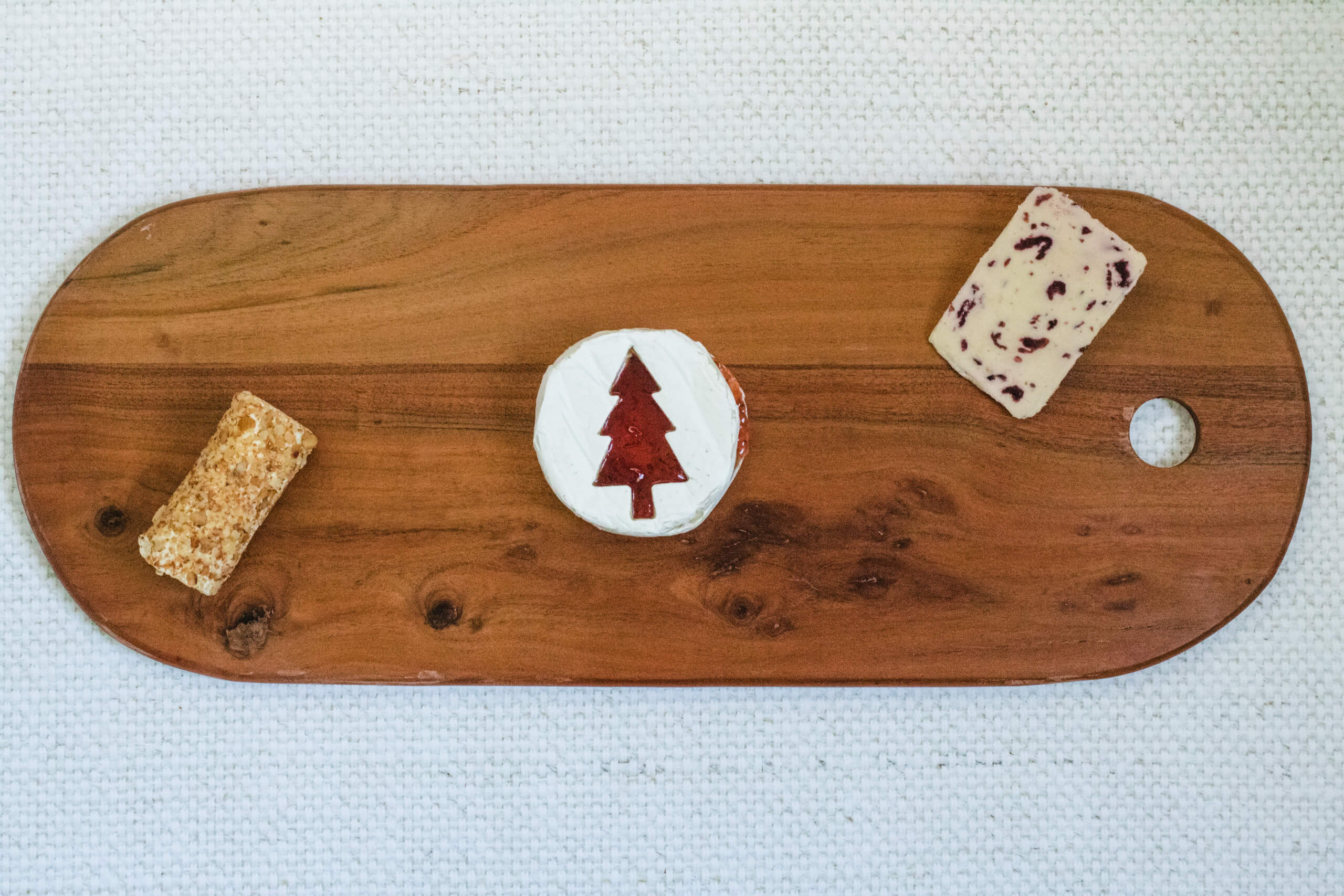Charcuterie board with the Brie with a Christmas tree cut into it with strawberry jam filling the Christmas tree, wensleydale cheese and apple and cinnamon cheese placed on the board. 