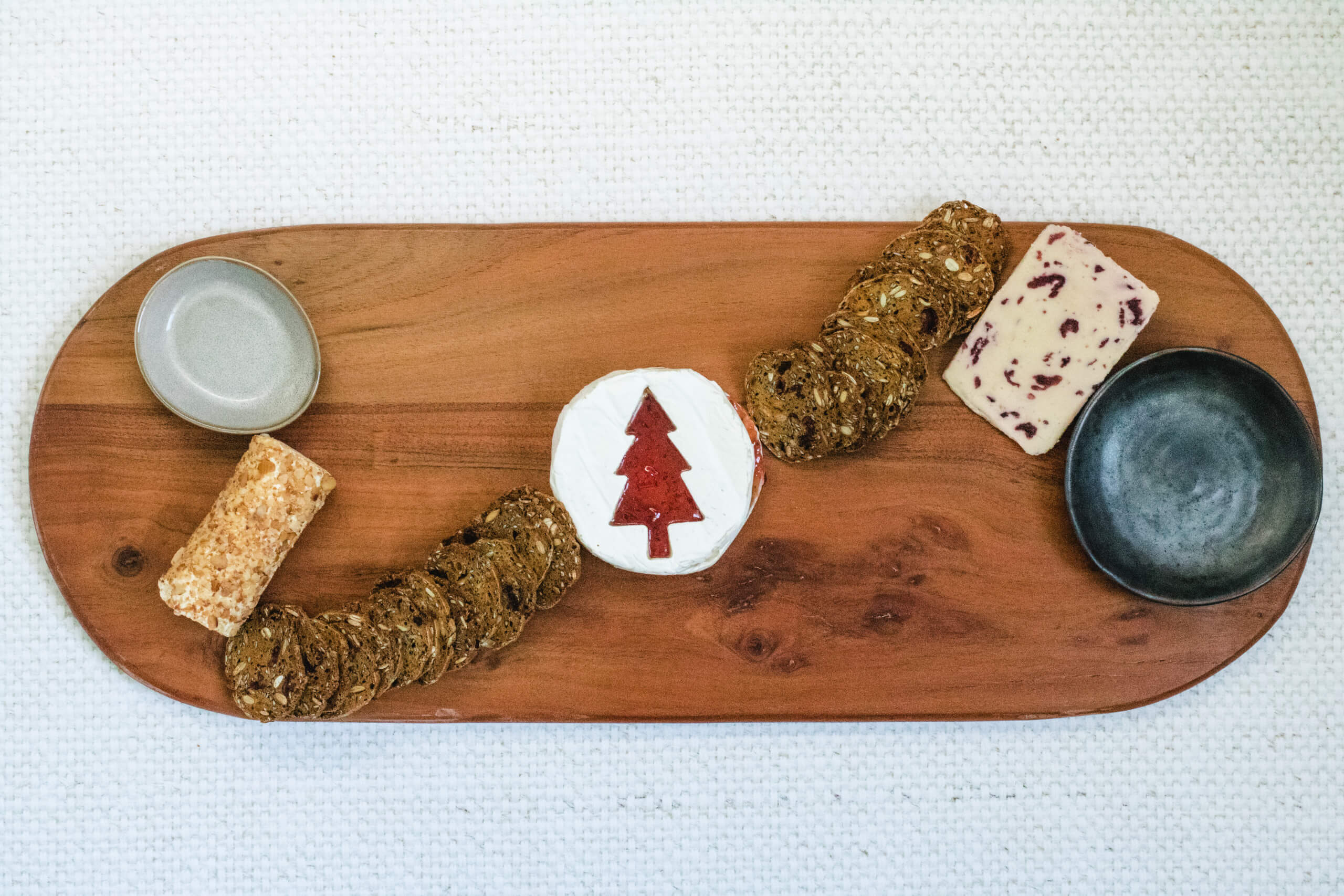 Charcuterie board with the Brie with a Christmas tree cut into it with strawberry jam filling the Christmas tree, wensleydale cheese and apple and cinnamon cheese placed on the board and a line of crackers from the cheese. 