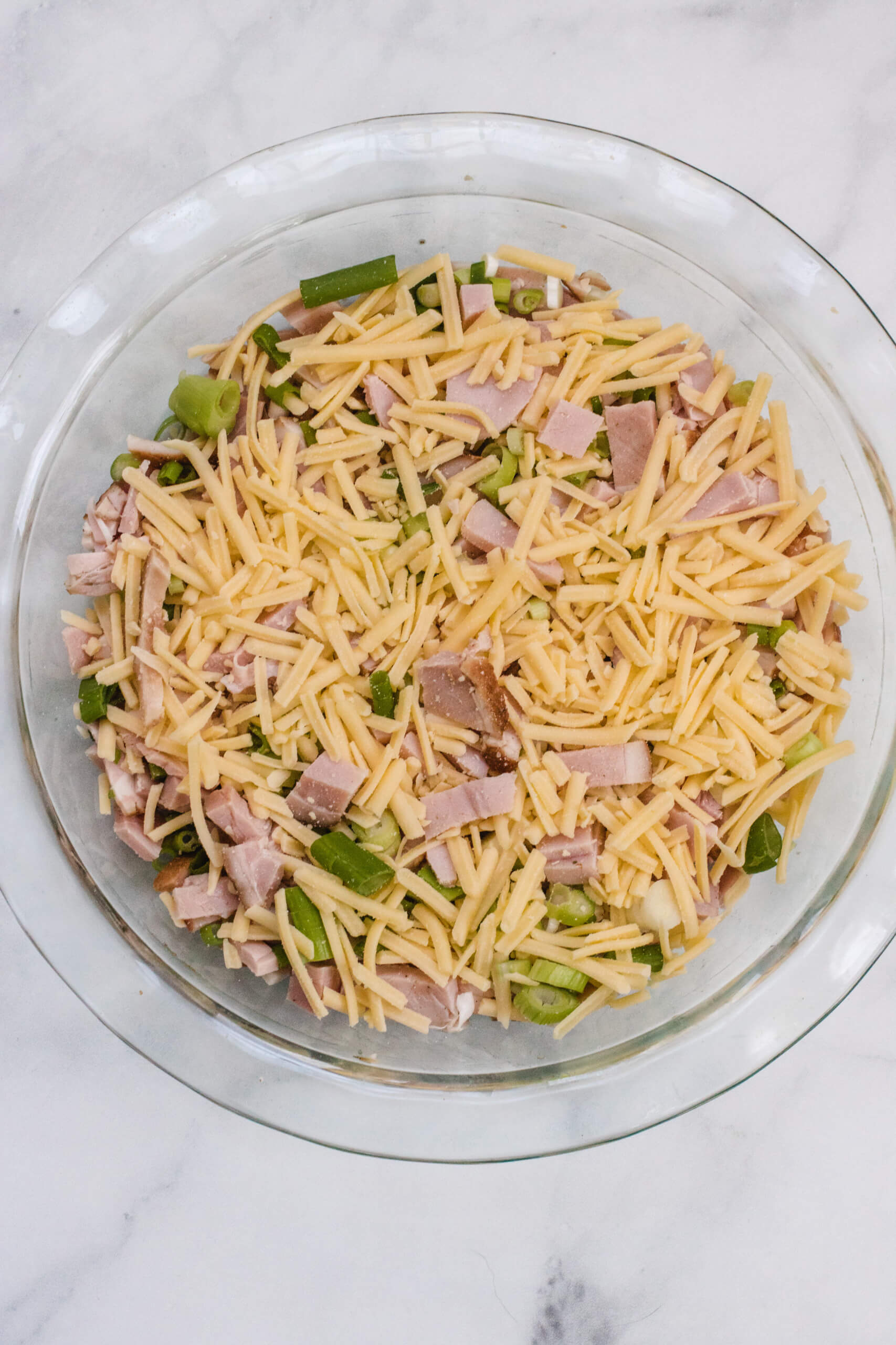 Ham, cheese and spring onion in the baking dish in a pie dish on a marble white background. 