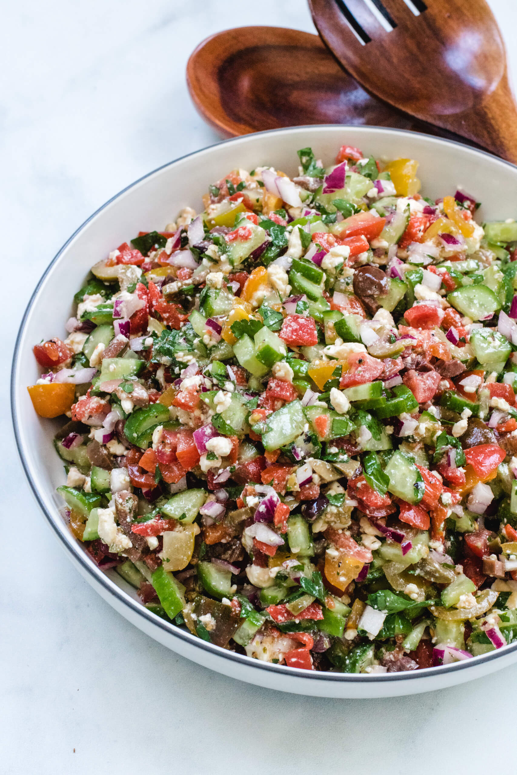 Mediterranean chopped salad in a large salad bowl with wooden spoons beside it