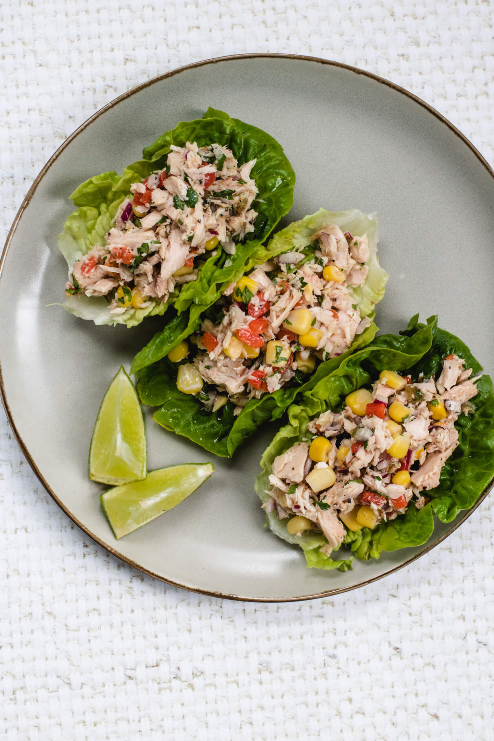 Mexican tuna salad in lettuce cups with a side of lime wedges on a light grey place. 