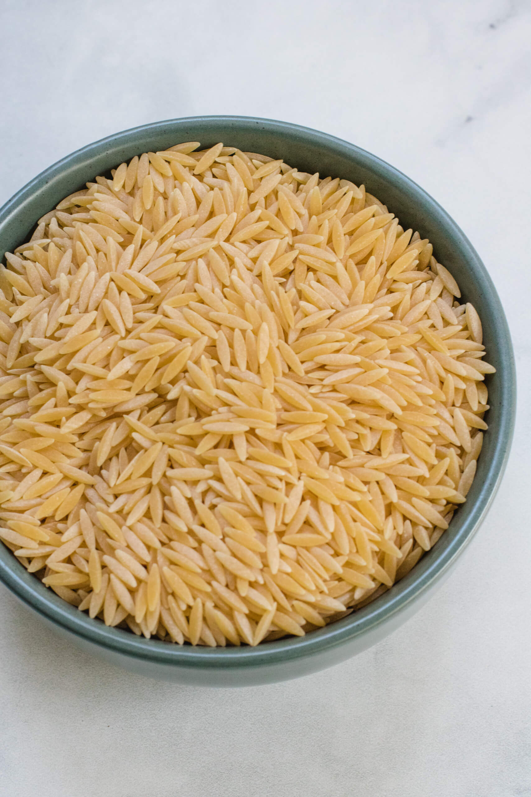 Orzo in a green bowl on a white background