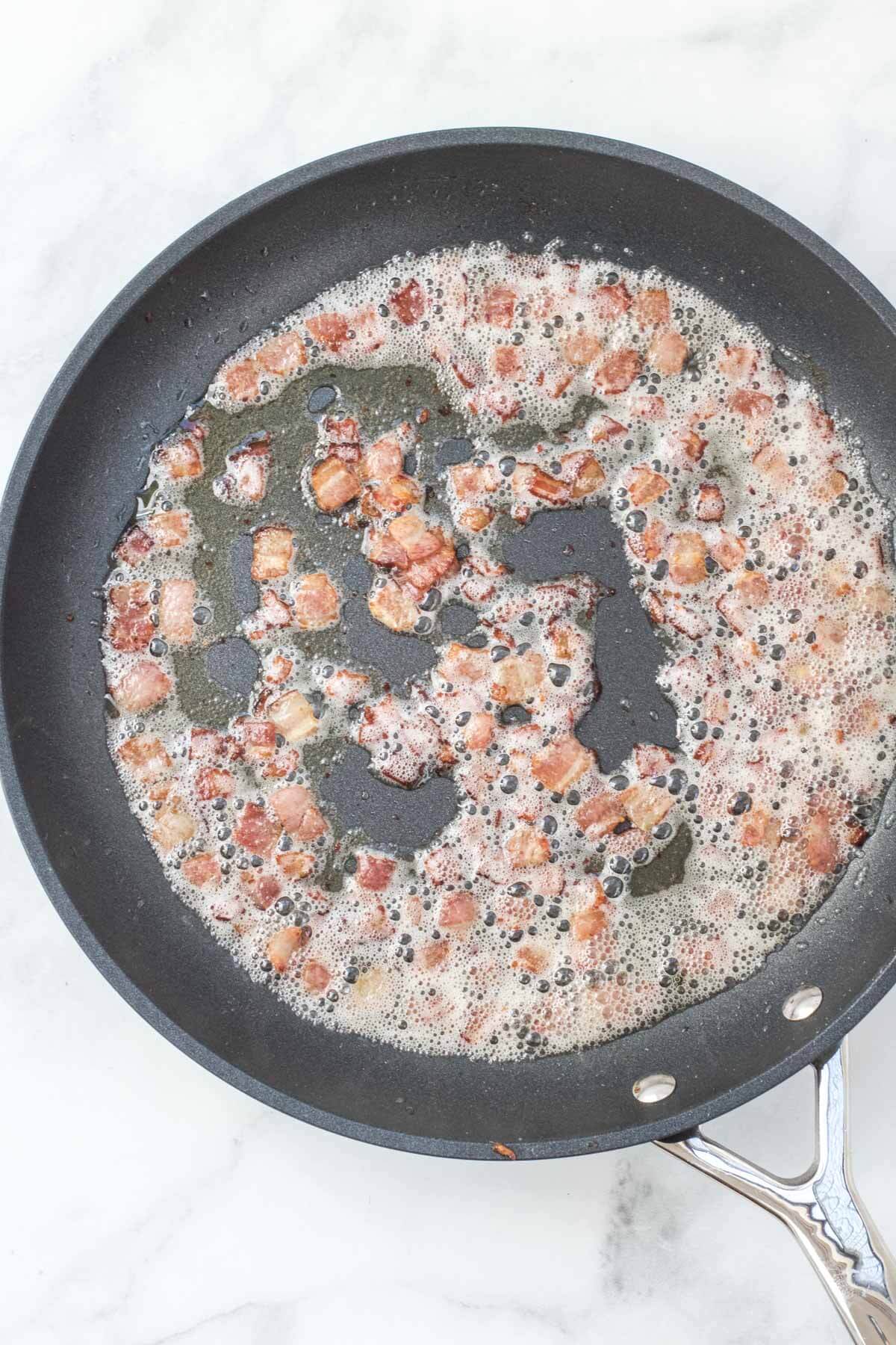 Bacon frying in a skillet. It has browned and realeased the bacon grease.