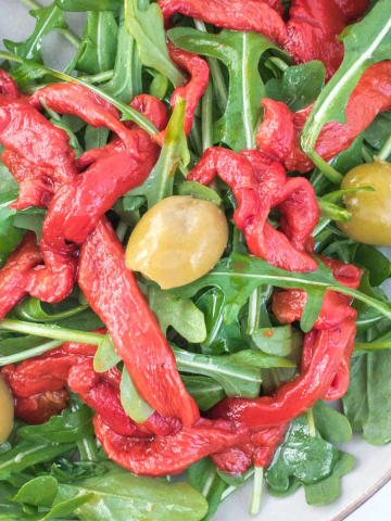 Roasted bell pepper strips on a bed of arugula with olives.
