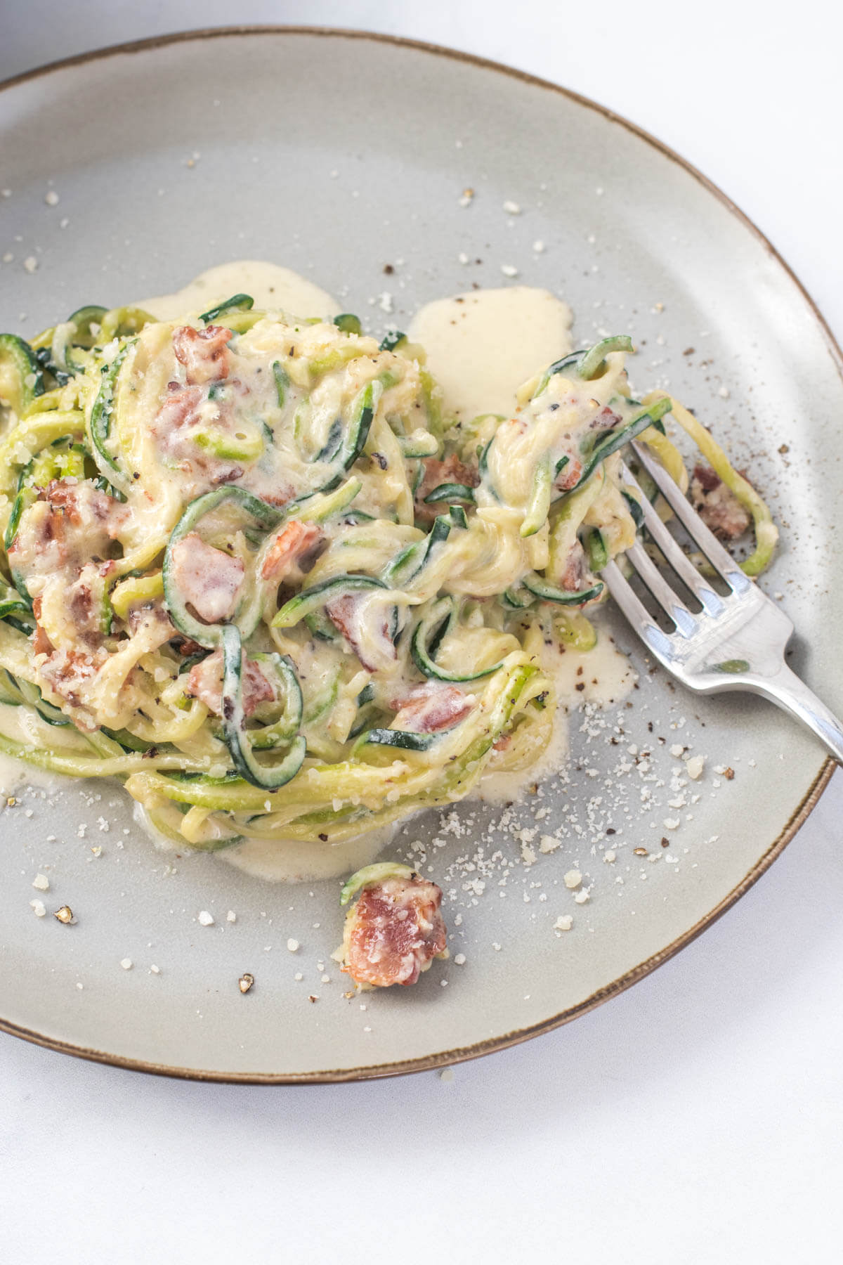 Zucchini noodles in carbonara sauce on a plate with a fork about to take a bite.